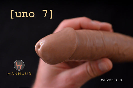 A hand holding a realistic silicone penis sleeve labeled "uno 7" by MANHUUD