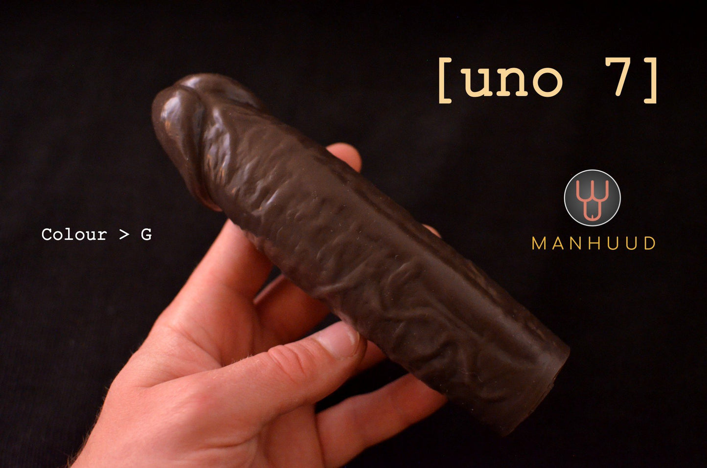 A hand holding a dark-colored MANHUUD "uno 7" silicone penis sleeve