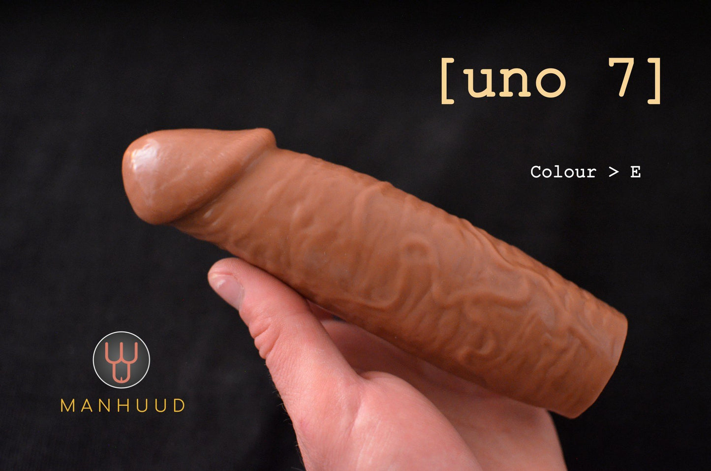 A hand holding a brown MANHUUD "uno 7" silicone penis sleeve