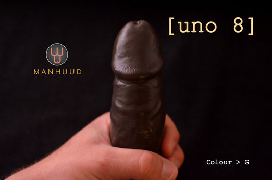 A hand holding a dark-colored MANHUUD "uno 8" silicone penis sleeve