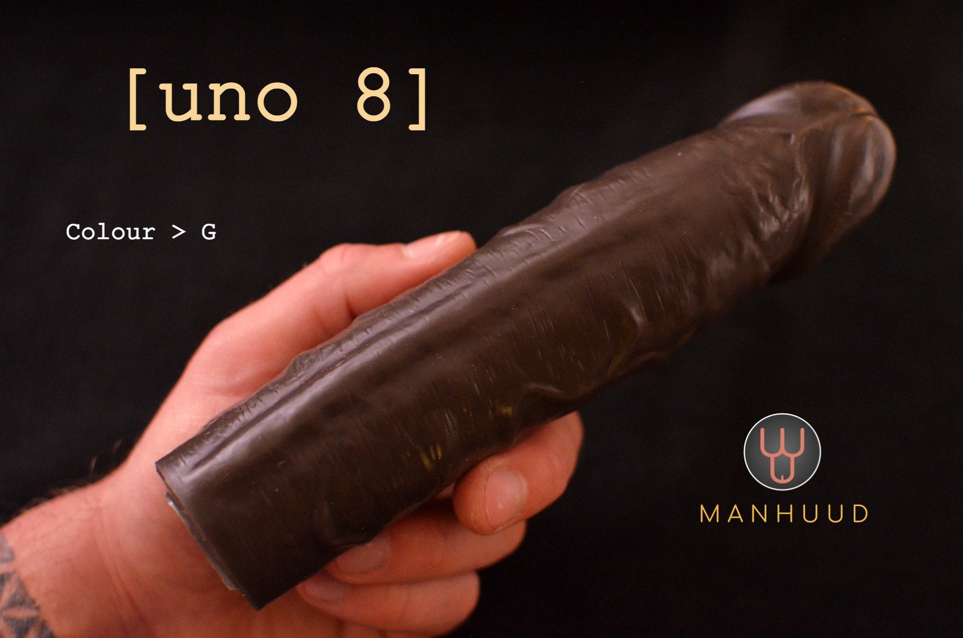 A hand holding a dark-colored MANHUUD "uno 8" silicone penis sleeve