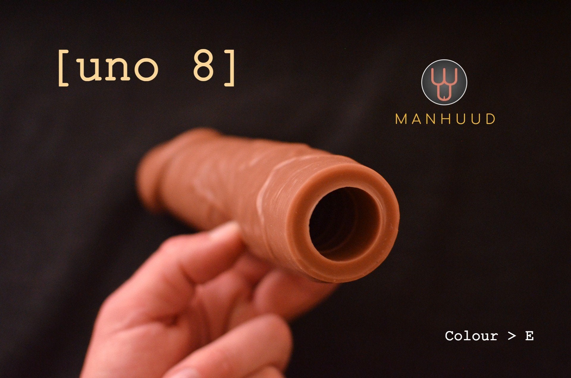 A hand holding a brown MANHUUD "uno 8" silicone penis sleeve, showing the open end