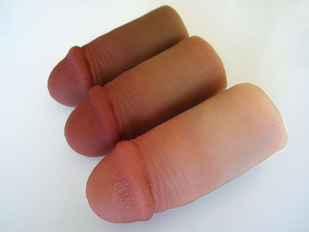 Three realistic, flesh-toned silicone dildos in different shades, lined up side by side on a white surface