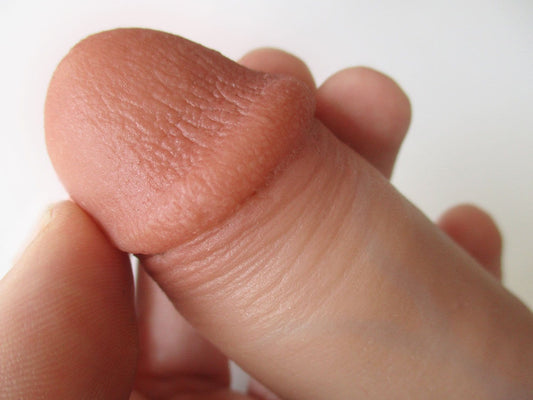 Close-up of a hand holding the tip of a realistic, flesh-toned silicone dildo, showing detailed texture