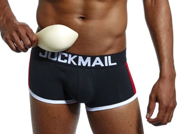 A model in black Jockmail underwear holding a protective cup against his groin