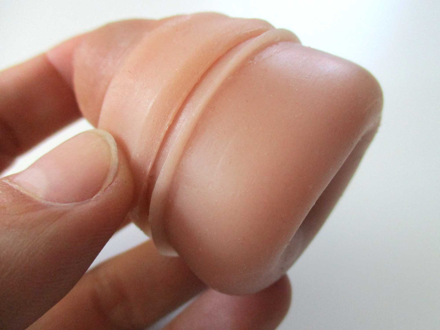 A hand holding a flesh-toned silicone sleeve, showing its smooth, rounded tip and ribbed design