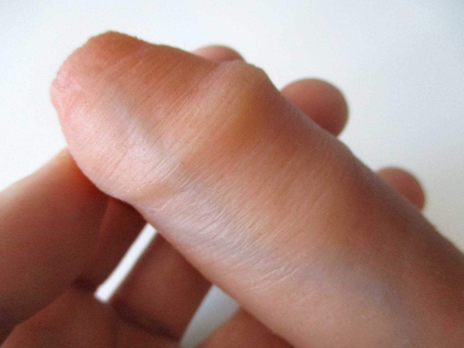A hand holding a flesh-toned silicone sleeve, showing its smooth, rounded tip and ribbed design