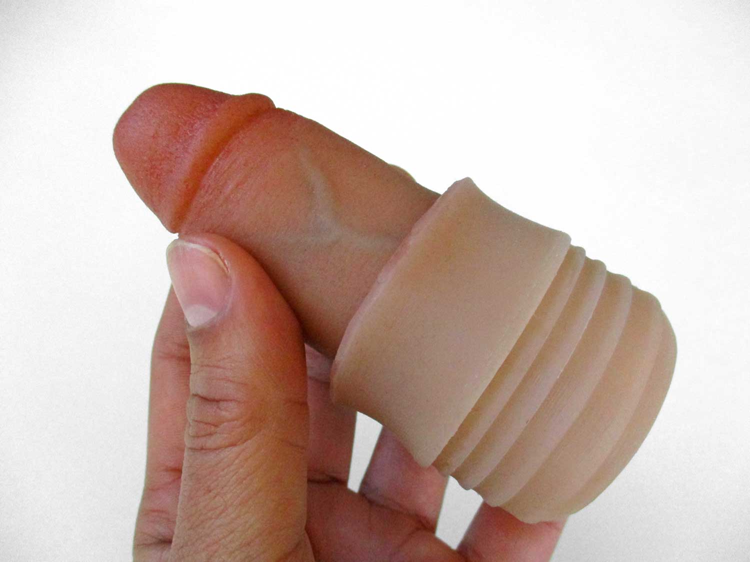 A hand holding a realistic, flesh-toned silicone dildo with a ribbed, detachable sleeve near the base