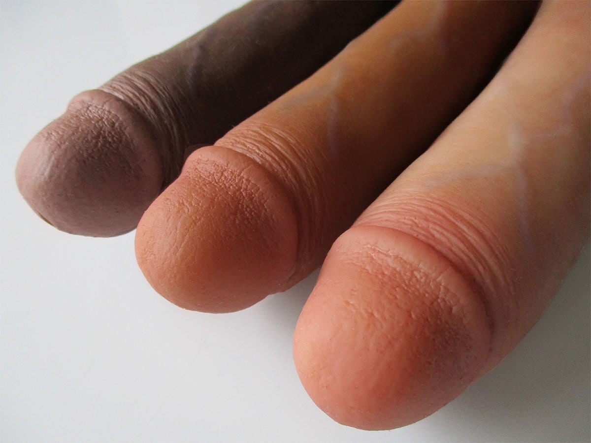 Close-up of three realistic silicone dildos in different skin tones, lined up side by side